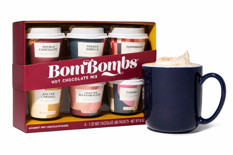BomBombs hot chocolate sampler gift box with six flavored packets and a navy mug of whipped hot chocolate.